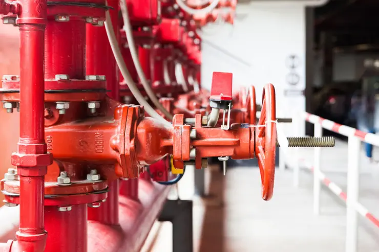 Row of red industrial pipes with large handwheel valves and metallic fittings, likely part of a fire protection or sprinkler system, installed in a building utility area.<br />
