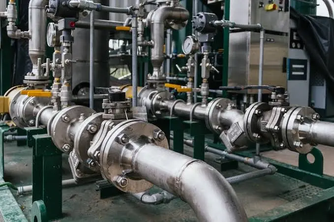 Complex stainless steel piping system mounted on a green frame, featuring valves, gauges, and interconnected flanges for fluid regulation.<br />
