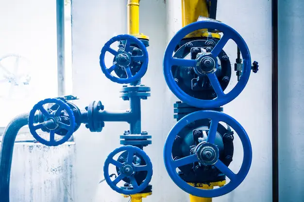 Close-up of an industrial piping system with several blue wheel-handled valves attached to yellow pipes, used for fluid control.<br />
