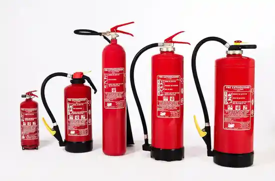 Row of five red fire extinguishers of varying sizes with black hoses, pressure gauges, and red handles. Labels show usage instructions and fire classification symbols.